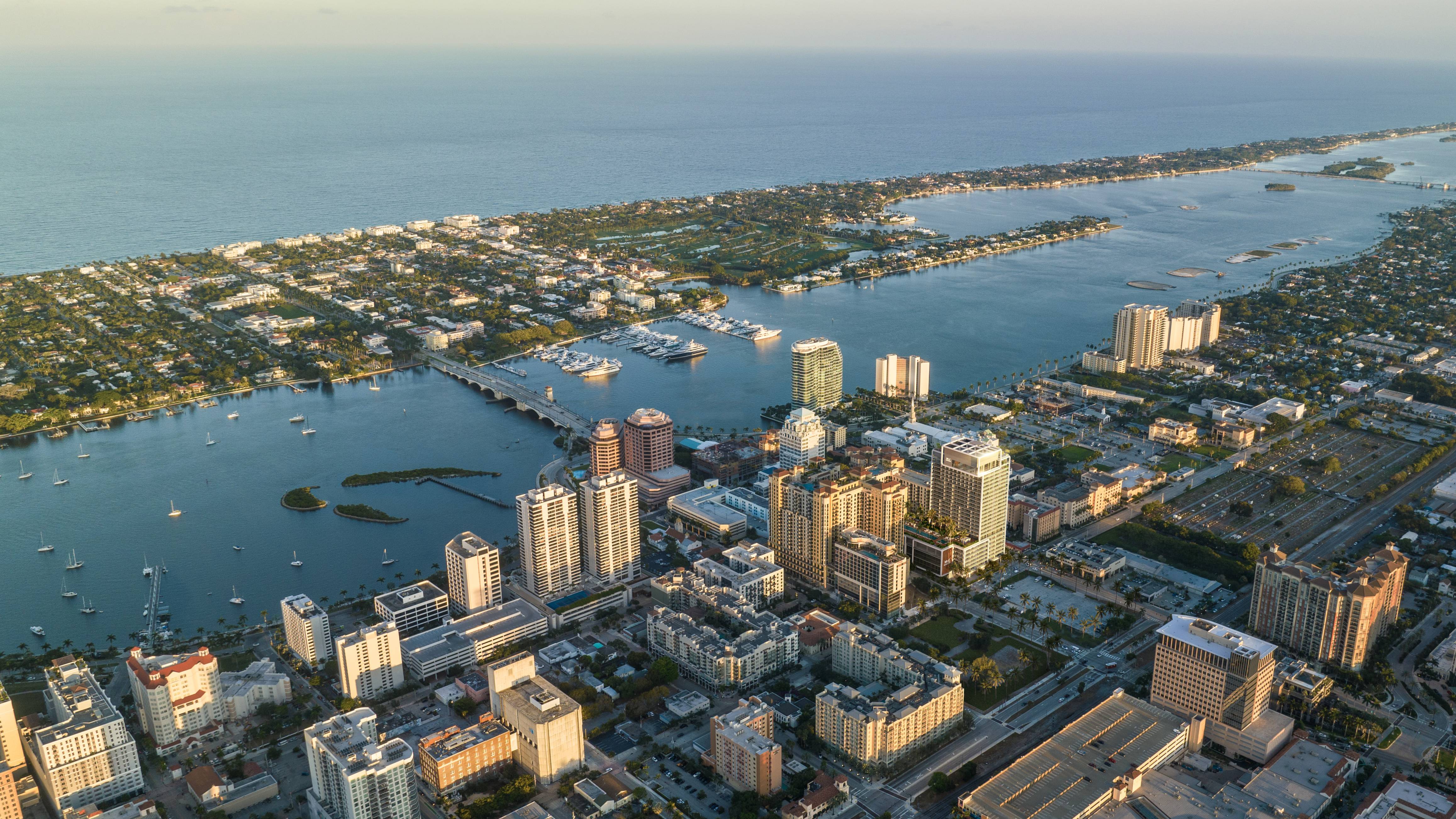 Mr. C Residences West Palm Beach aerial waterfront cityscape at sunset, showcasing luxury and ultra luxury preconstruction condos along the coast.