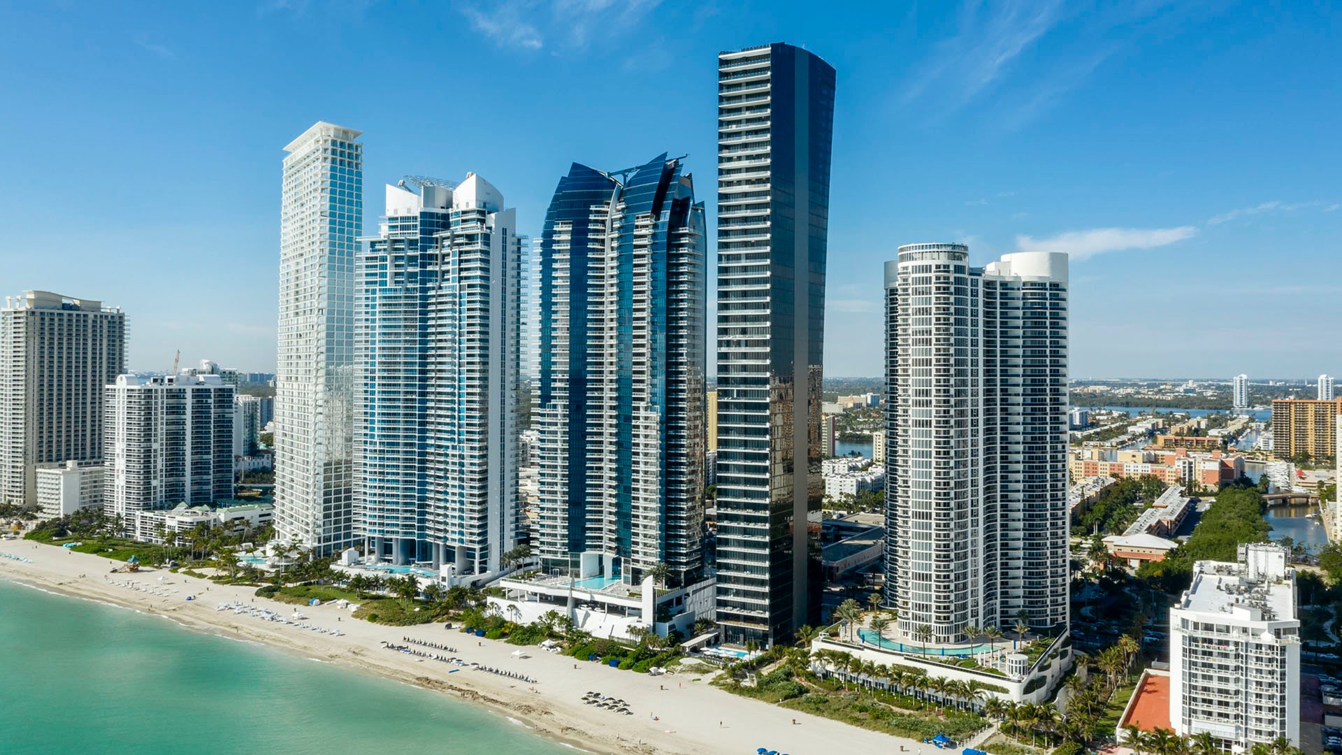Coastal aerial of Muse Residences in Sunny Isles Beach along the beachfront skyline, showing luxury and ultra luxury condos set between the sandy shore and the city.