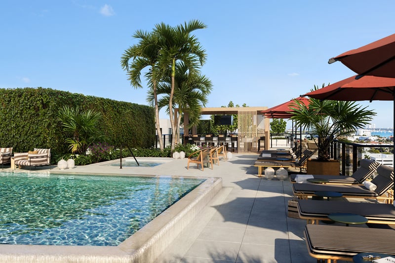 Rooftop pool deck at Nora House in West Palm Beach, luxury and ultra luxury condos with red umbrellas, striped loungers, a pergola lounge, tropical landscaping, and open water views beyond the terrace.