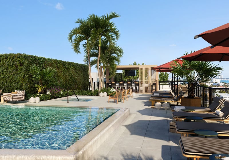 Rooftop pool deck at Nora House in West Palm Beach, luxury and ultra luxury condos with red umbrellas, striped loungers, a pergola lounge, tropical landscaping, and open water views beyond the terrace.