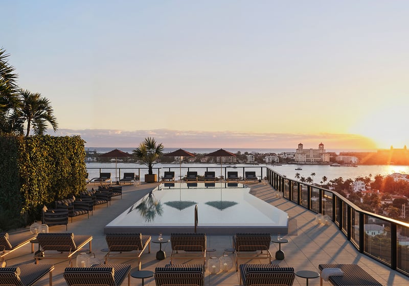 Sunset rooftop pool terrace at Nora House in West Palm Beach, luxury and ultra luxury condos featuring a serene rooftop pool, striped loungers, glass railings, and sweeping waterfront views at golden hour.