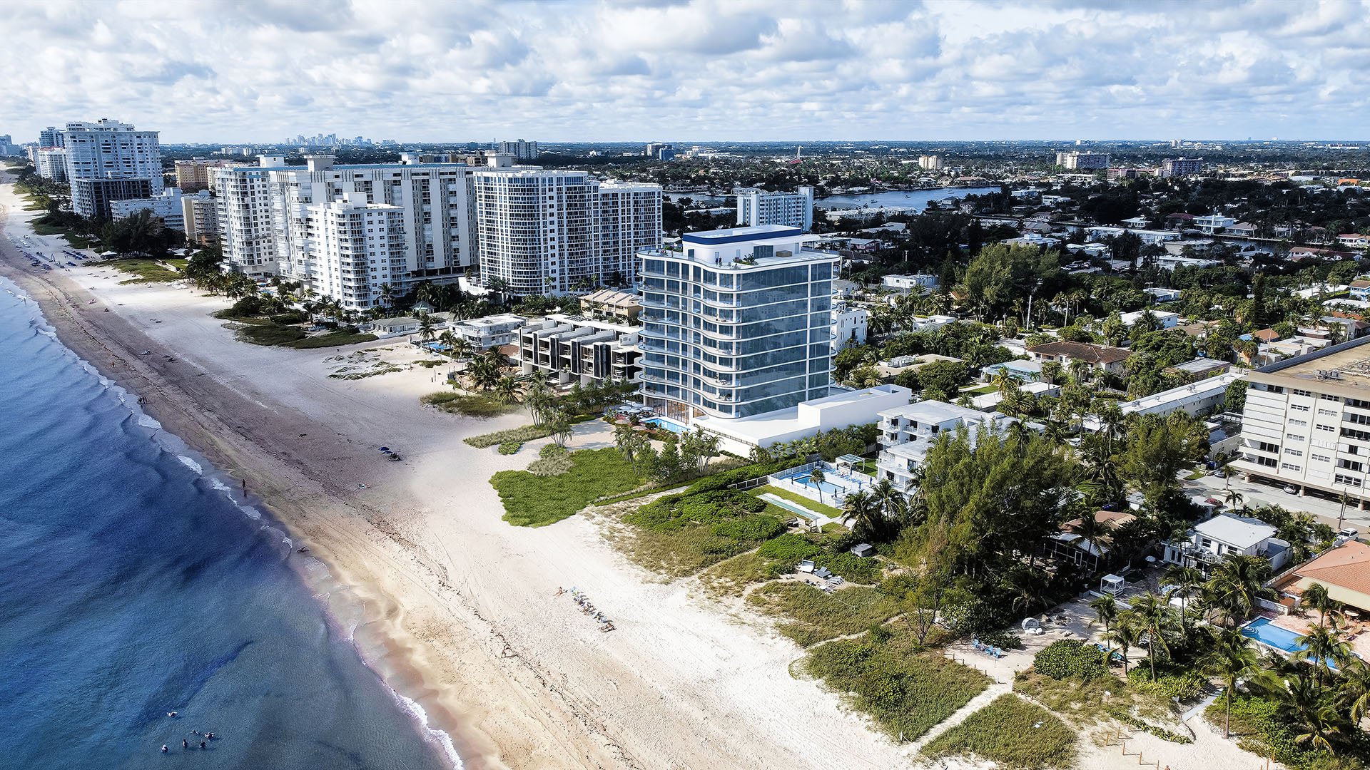 Aerial view of Ocean 580 in Pompano Beach, preconstruction luxury and ultra luxury condos with a curved beachfront tower, sandy shoreline, neighboring coastal high-rises and a sweeping ocean coastline.