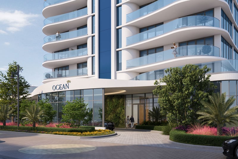 Daytime entrance at Ocean 580 in Pompano Beach, preconstruction luxury and ultra luxury condos with curved glass balconies, a porte cochere driveway, landscaped planting beds and a modern lobby frontage.