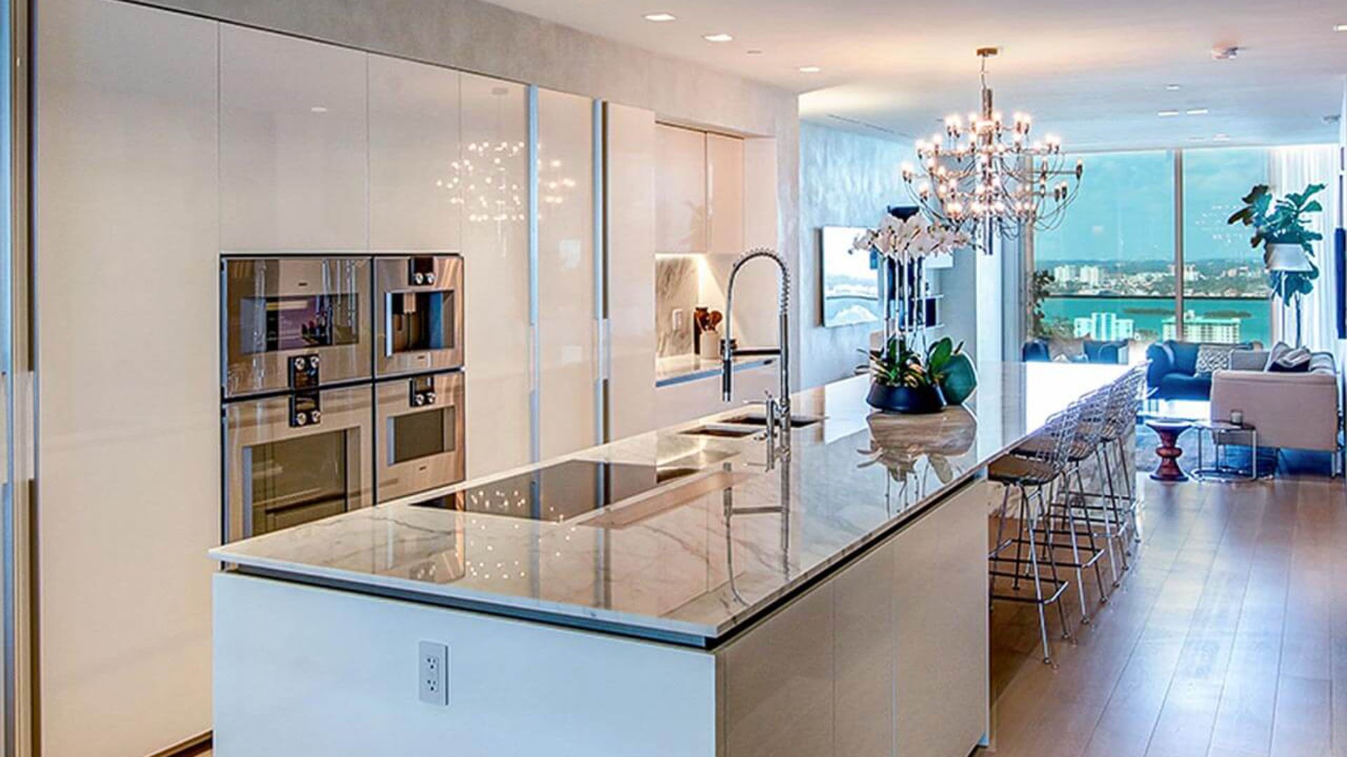 Chef kitchen with a long waterfall island, built in appliances and bay views into the living area at Oceana Bal Harbour in Bal Harbour, Florida, capturing the luxury interiors of these ultra luxury condos.