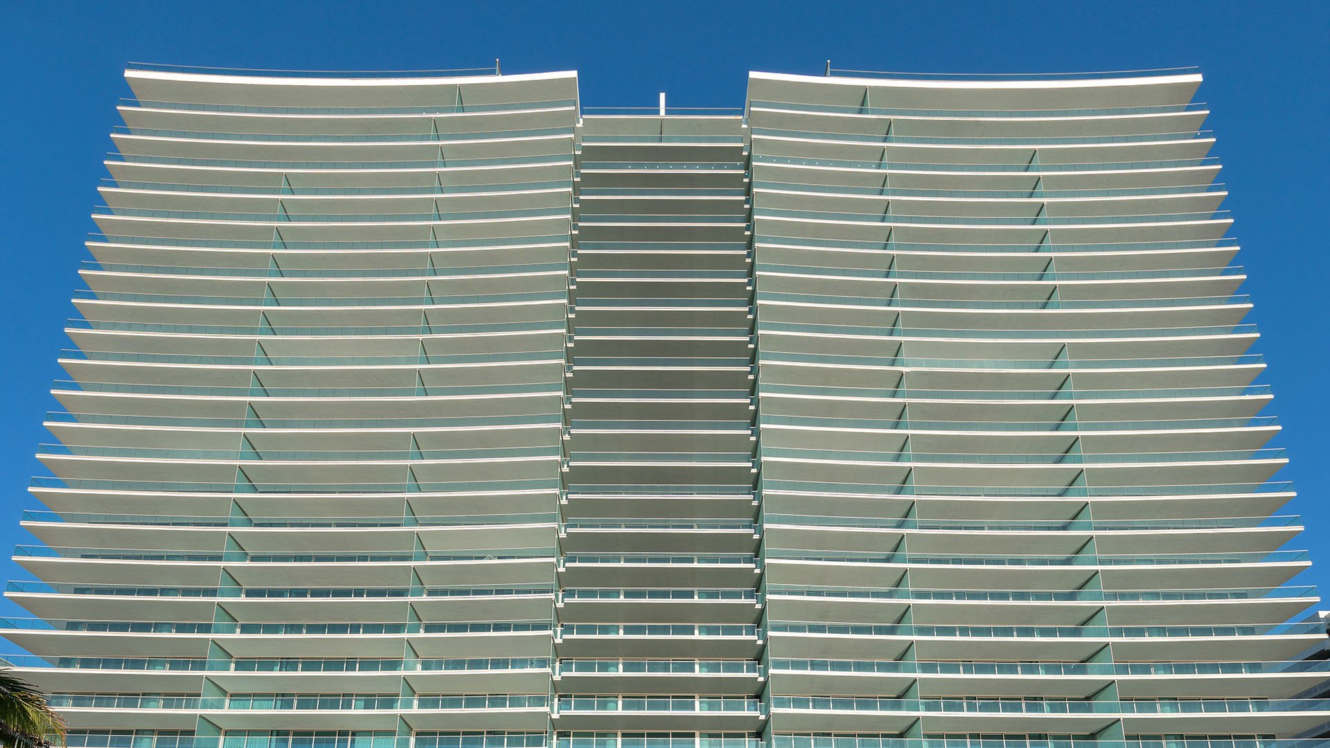 Curved condo exterior with sweeping glass balconies rising against a clear blue sky at Oceana Bal Harbour in Bal Harbour, Florida, emphasizing the luxury architecture of these ultra luxury condos.