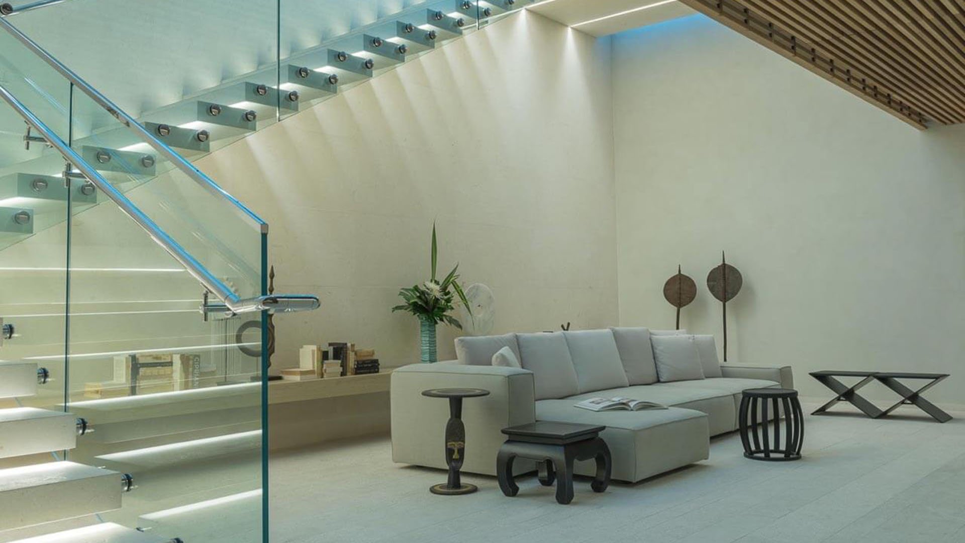 Minimalist lounge beneath a glass staircase with a sectional sofa and sculptural tables at Oceana Bal Harbour in Bal Harbour, Florida, showcasing the serene luxury interiors of these ultra luxury condos.