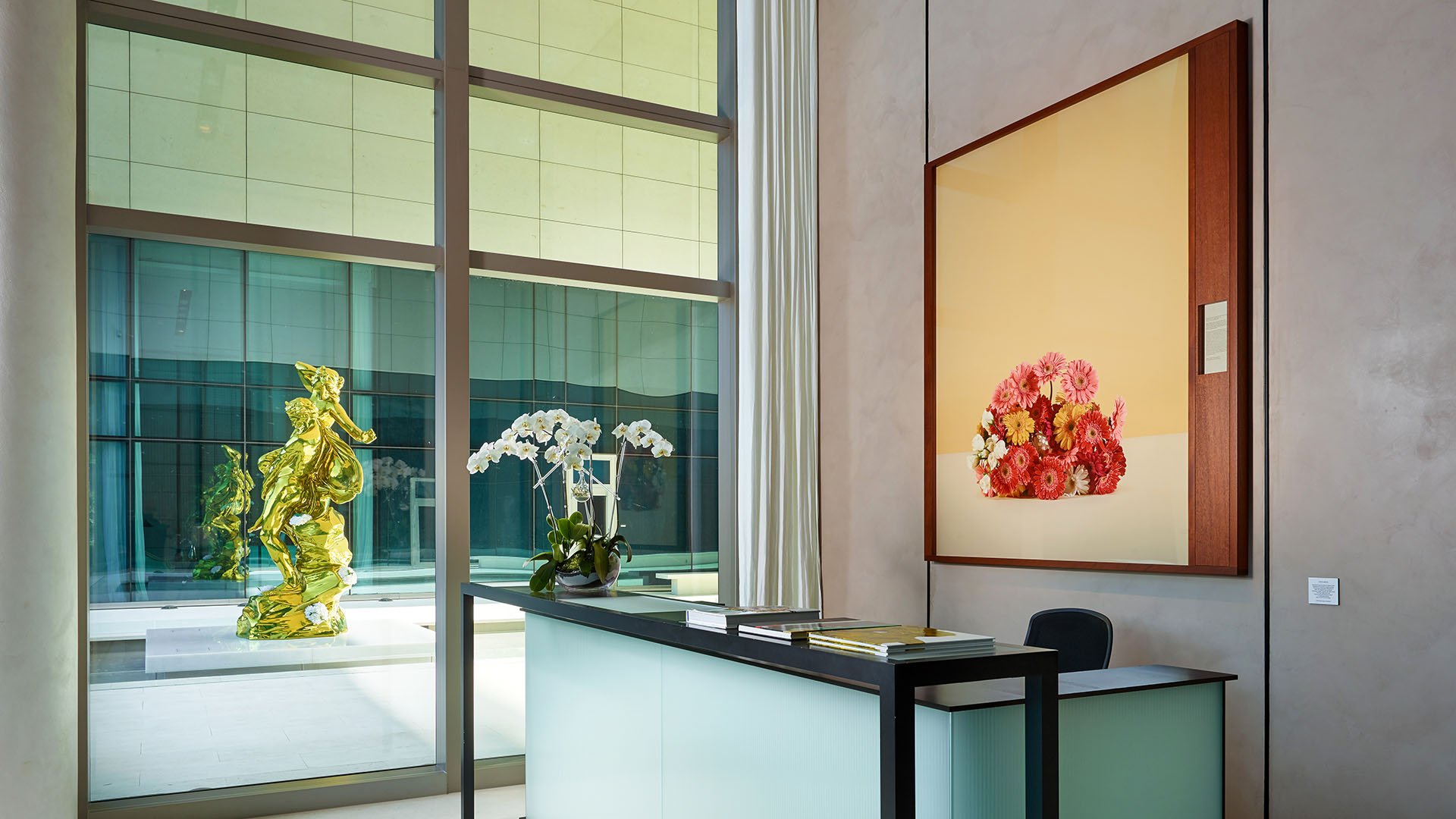 Reception desk with floral artwork, orchid arrangement and a sculpture courtyard view at Oceana Bal Harbour in Bal Harbour, Florida, reflecting the polished luxury welcome of these ultra luxury condos.