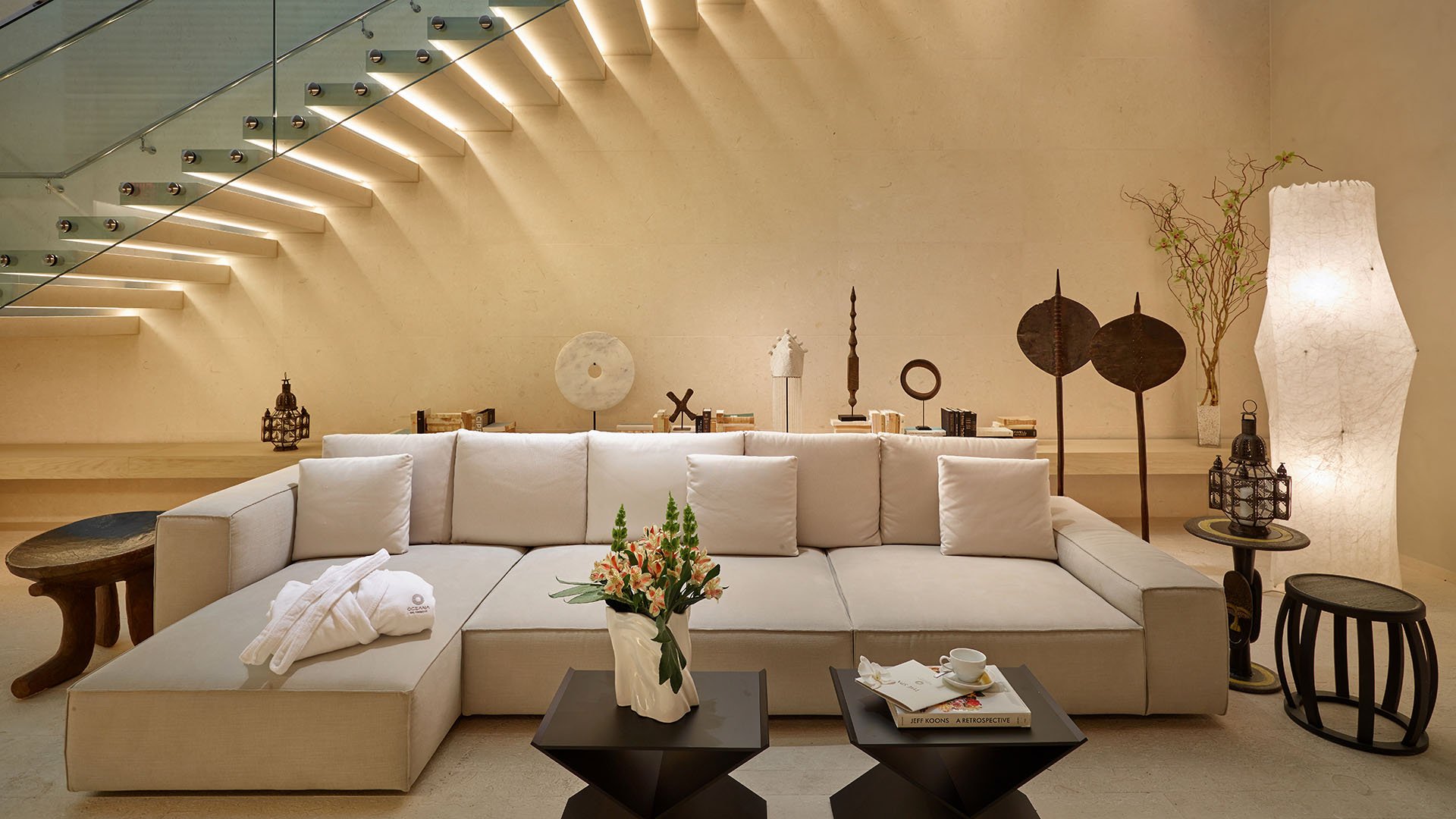 Spa lounge with a sectional sofa tucked beneath an illuminated glass stair at Oceana Bal Harbour in Bal Harbour, Florida, expressing the calming luxury wellness spaces within these ultra luxury condos.