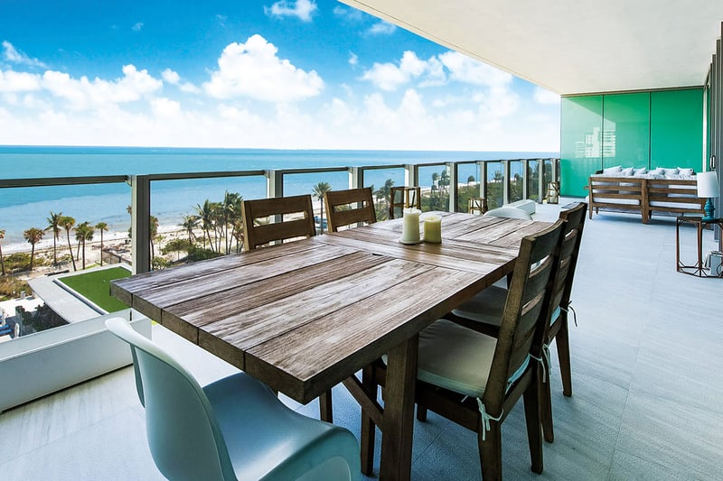 Beachfront dining terrace at Oceana Key Biscayne in Key Biscayne, showing luxury and ultra luxury condos with a long covered balcony, outdoor dining table, lounge seating, and sweeping ocean views.