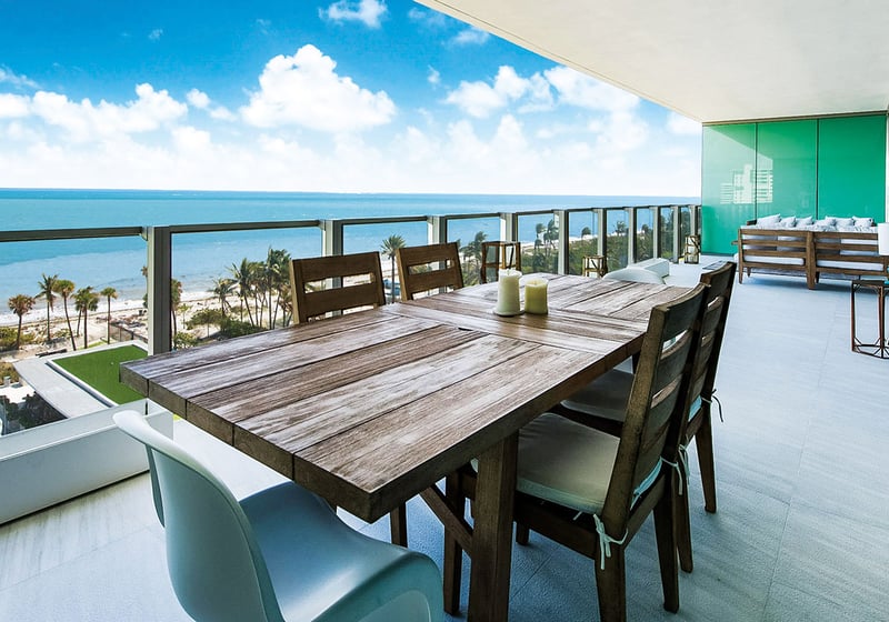 Beachfront dining terrace at Oceana Key Biscayne in Key Biscayne, showing luxury and ultra luxury condos with a long covered balcony, outdoor dining table, lounge seating, and sweeping ocean views.