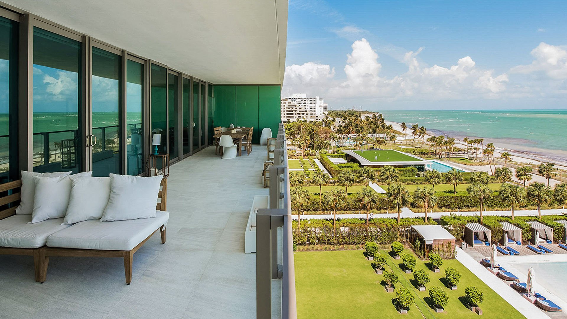 Corner balcony at Oceana Key Biscayne in Key Biscayne, where luxury and ultra luxury condos overlook manicured grounds, pool cabanas, palm-lined lawns, the shoreline, and turquoise water.
