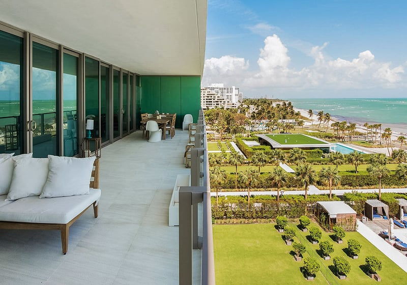 Corner balcony at Oceana Key Biscayne in Key Biscayne, where luxury and ultra luxury condos overlook manicured grounds, pool cabanas, palm-lined lawns, the shoreline, and turquoise water.