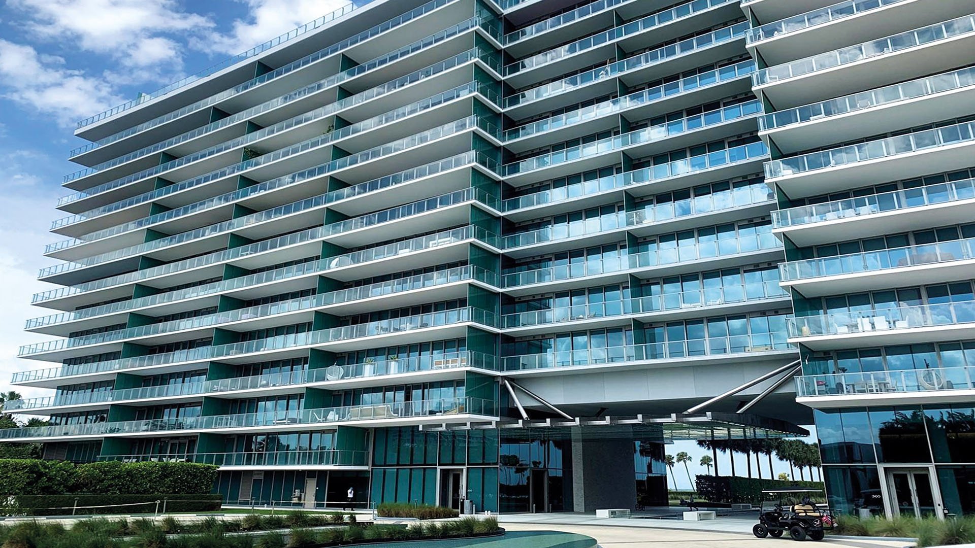 Street-level exterior of Oceana Key Biscayne in Key Biscayne, highlighting luxury and ultra luxury condos with curving glass balconies, a sleek coastal facade, and landscaped arrival areas.