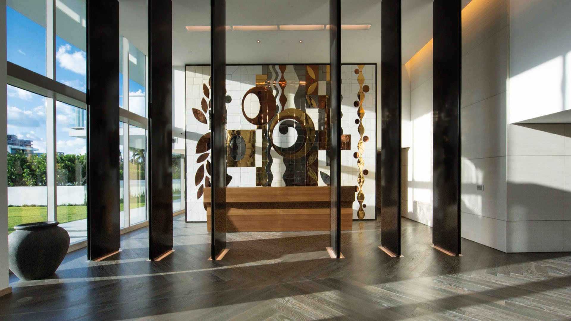 Lobby interior at Oceana Key Biscayne in Key Biscayne, where luxury and ultra luxury condos feature soaring ceilings, floor-to-ceiling glass, dark wood accents, and a large art installation.
