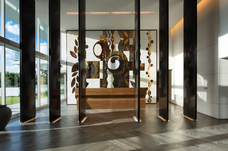 Lobby interior at Oceana Key Biscayne in Key Biscayne, where luxury and ultra luxury condos feature soaring ceilings, floor-to-ceiling glass, dark wood accents, and a large art installation.