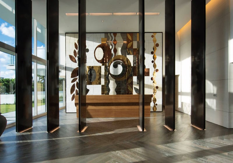 Lobby interior at Oceana Key Biscayne in Key Biscayne, where luxury and ultra luxury condos feature soaring ceilings, floor-to-ceiling glass, dark wood accents, and a large art installation.