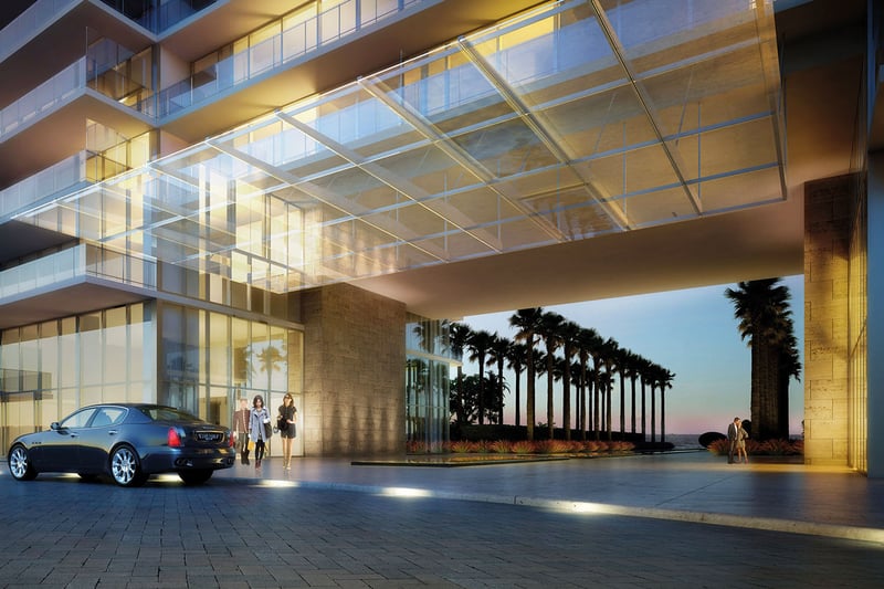 Dusk porte cochere at Oceana Key Biscayne in Key Biscayne, showcasing luxury and ultra luxury condos with a dramatic glass canopy, illuminated arrival court, palm-lined drive, and ocean beyond.