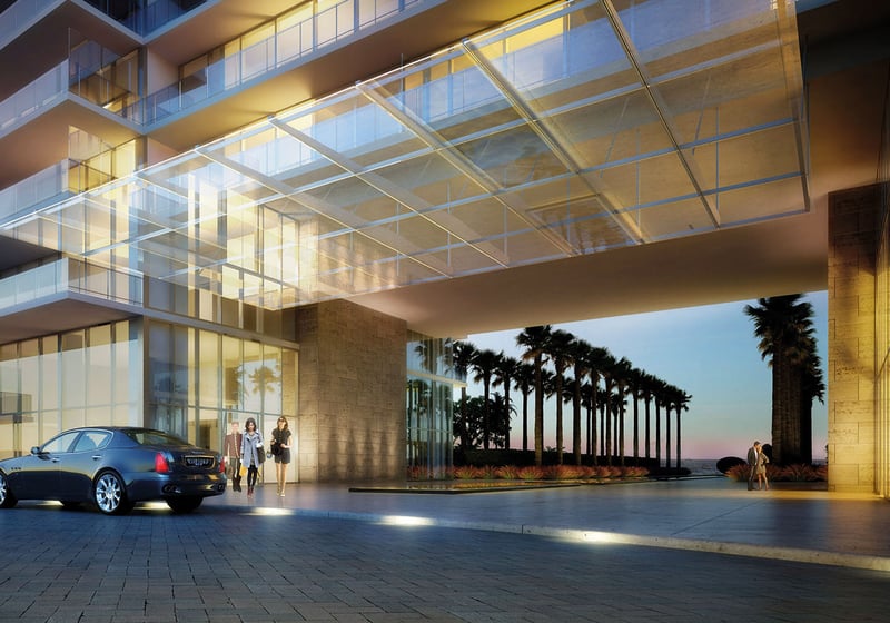 Dusk porte cochere at Oceana Key Biscayne in Key Biscayne, showcasing luxury and ultra luxury condos with a dramatic glass canopy, illuminated arrival court, palm-lined drive, and ocean beyond.