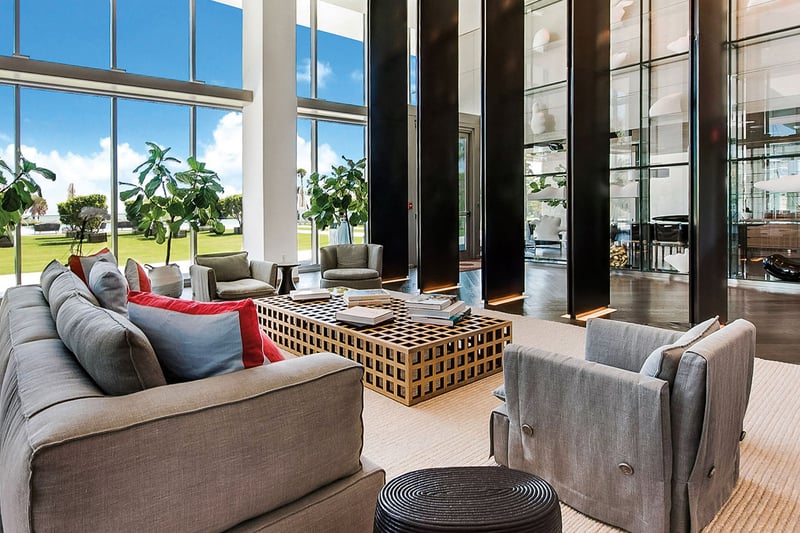 Glass-walled lobby lounge at Oceana Key Biscayne in Key Biscayne, featuring luxury and ultra luxury condos with expansive windows, modern seating, display shelving, and landscaped views.