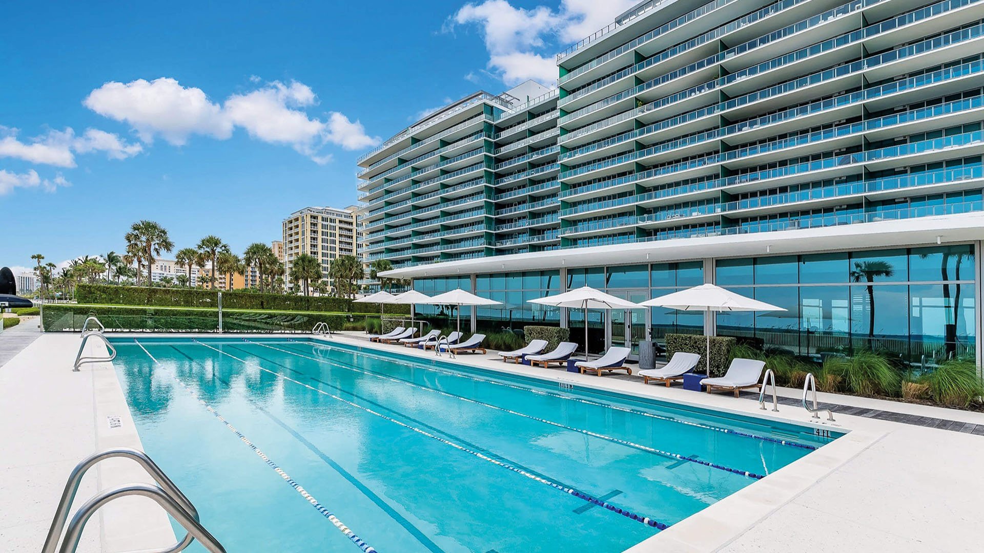 Lap pool at Oceana Key Biscayne in Key Biscayne, where luxury and ultra luxury condos line a sleek pool deck with umbrellas, loungers, reflective glass, and a curving exterior facade.