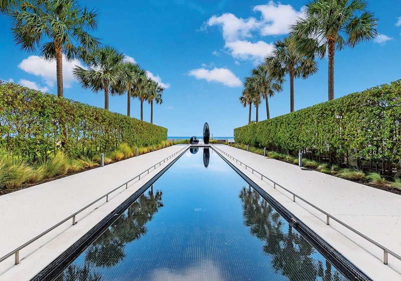 Palm-lined reflecting pool entry at Oceana Key Biscayne in Key Biscayne, showcasing luxury and ultra luxury condos with manicured hedges, sculpture, and a long water feature leading toward the ocean.