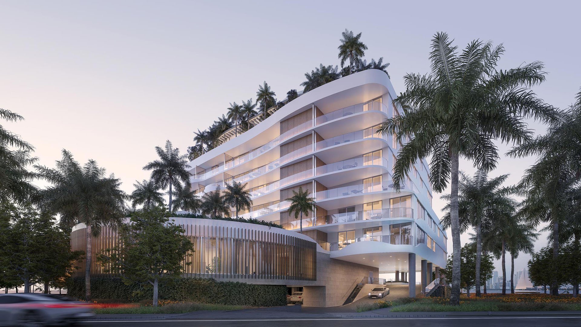 Onda Bay Harbor exterior street view at dusk in Bay Harbor Islands, Miami, Florida featuring curved modern architecture, balconies and palm-lined entrance-luxury and ultra luxury preconstruction condos.