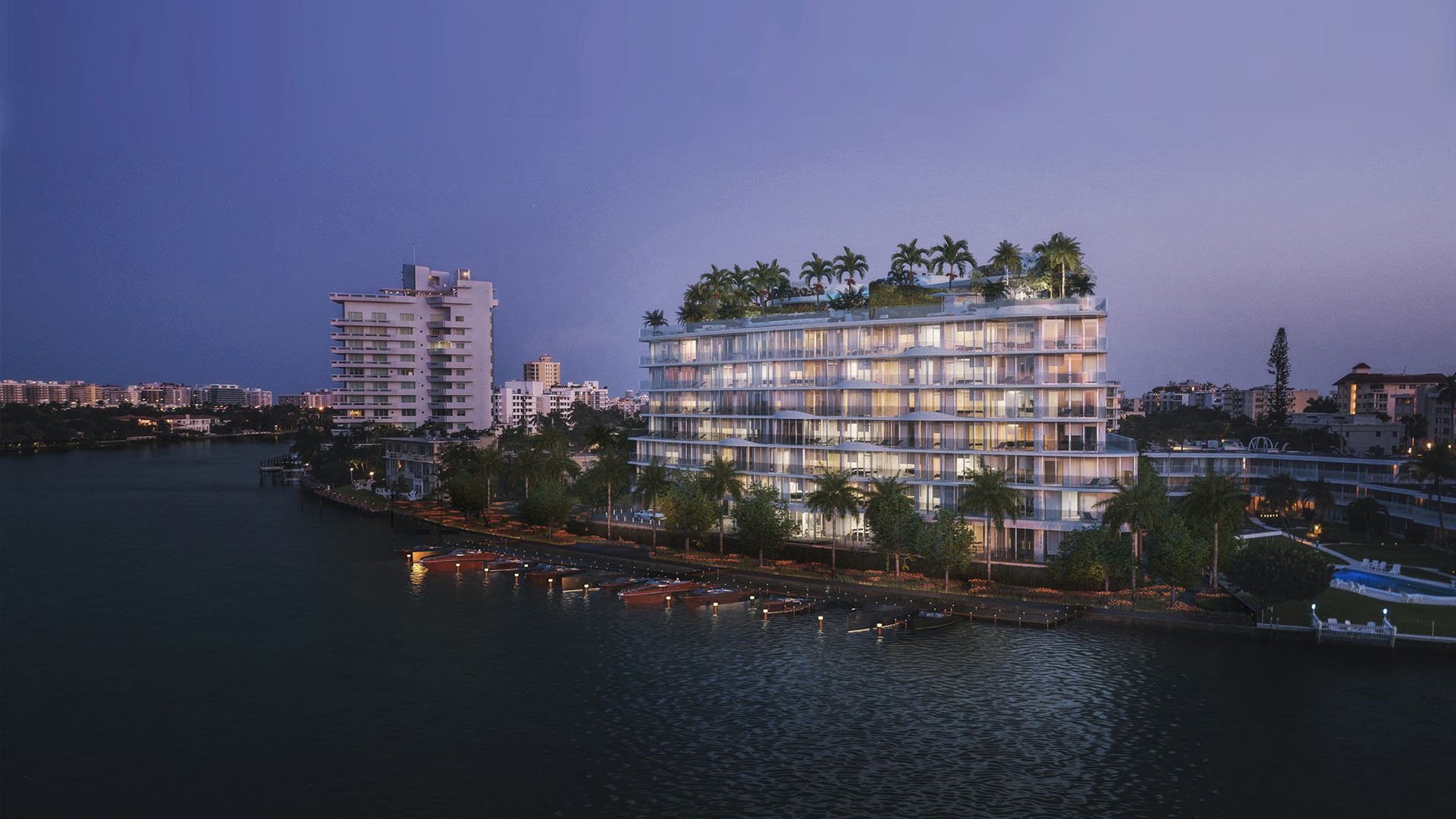 Night waterfront exterior of Onda, Bay Harbor Islands, Miami, Florida, with illuminated marina docks and rooftop palms, showcasing luxury and ultra luxury preconstruction waterfront condos on the bay.