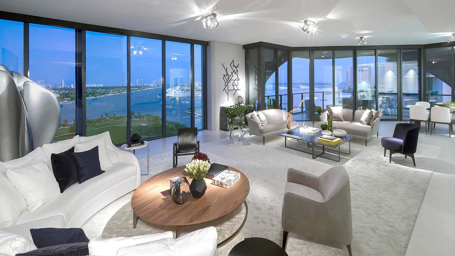 Corner living room at One Thousand Museum in Downtown Miami with plush seating, floor-to-ceiling glass, and twilight waterfront views for luxury and ultra luxury condos.