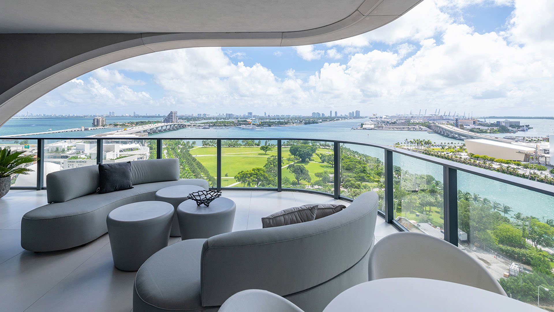 Curved terrace lounge at One Thousand Museum in Downtown Miami with rounded seating, green space below, and wide waterfront views for luxury and ultra luxury condos.