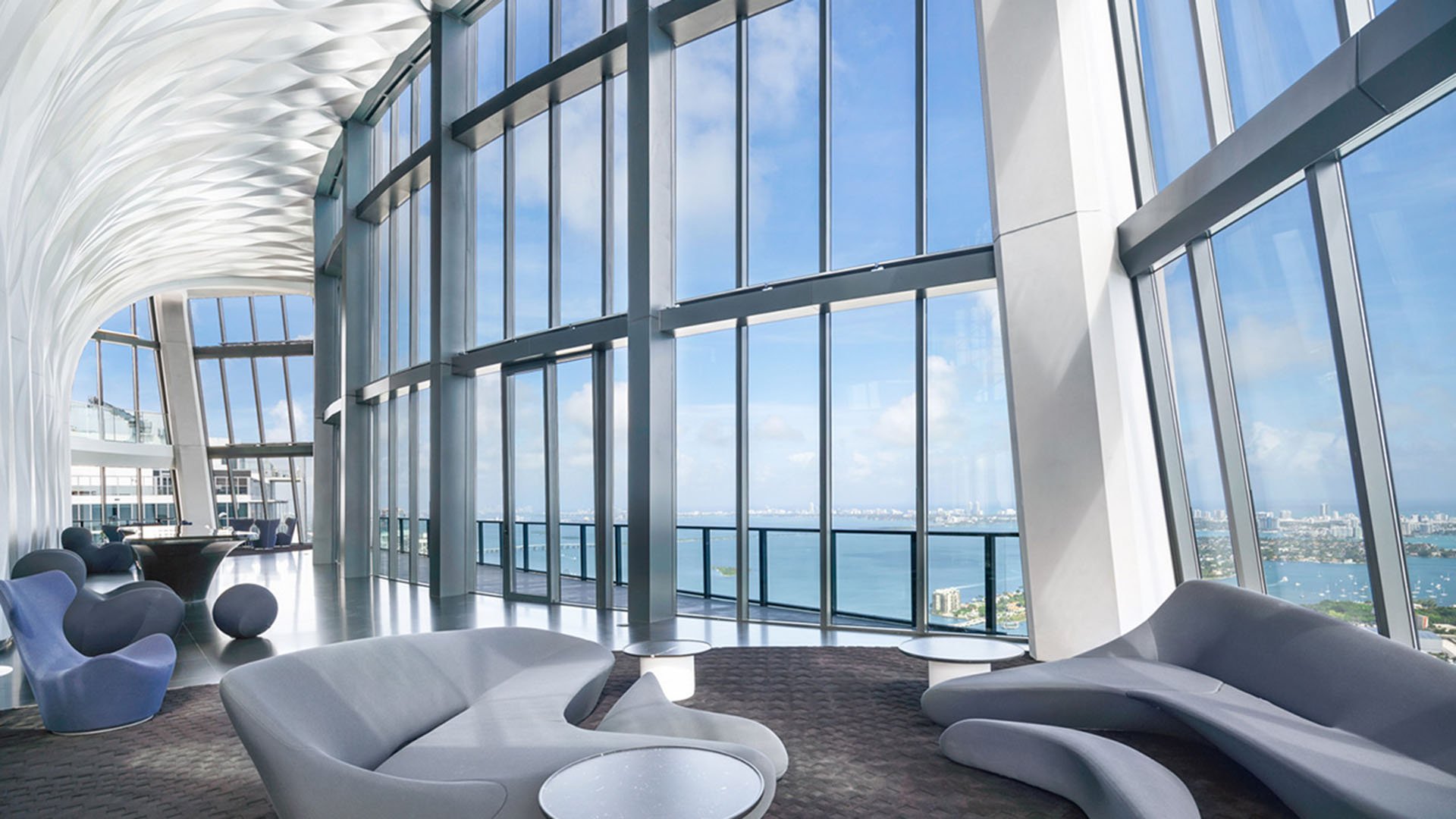 Double-height sky lounge at One Thousand Museum in Downtown Miami with a sculptural ceiling, curved seating, and tall glass facing the water for luxury and ultra luxury condos.