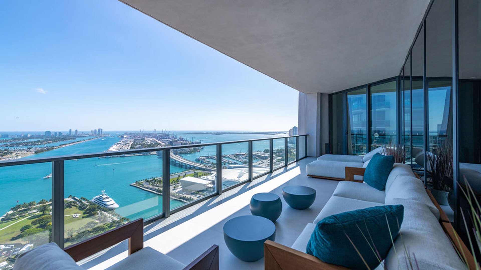 Expansive balcony lounge at One Thousand Museum in Downtown Miami with deep seating and long waterfront views, extending the living space of luxury and ultra luxury condos.
