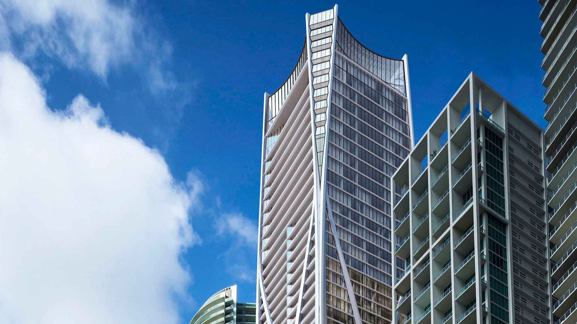 Looking up at the curved side facade of One Thousand Museum in Downtown Miami, emphasizing the vertical design of luxury and ultra luxury condos.