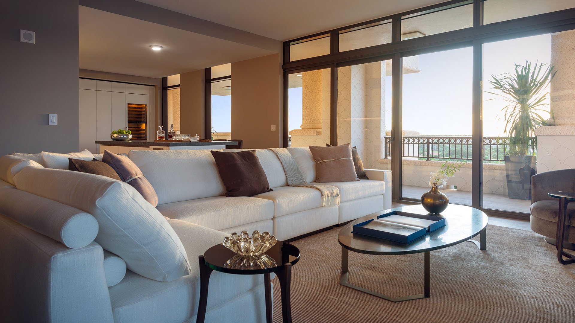 Balcony living room at Palazzo del Sol, Fisher Island, showcasing luxury and ultra luxury condos with a cream sectional, glass doors, and a furnished waterfront terrace just beyond.