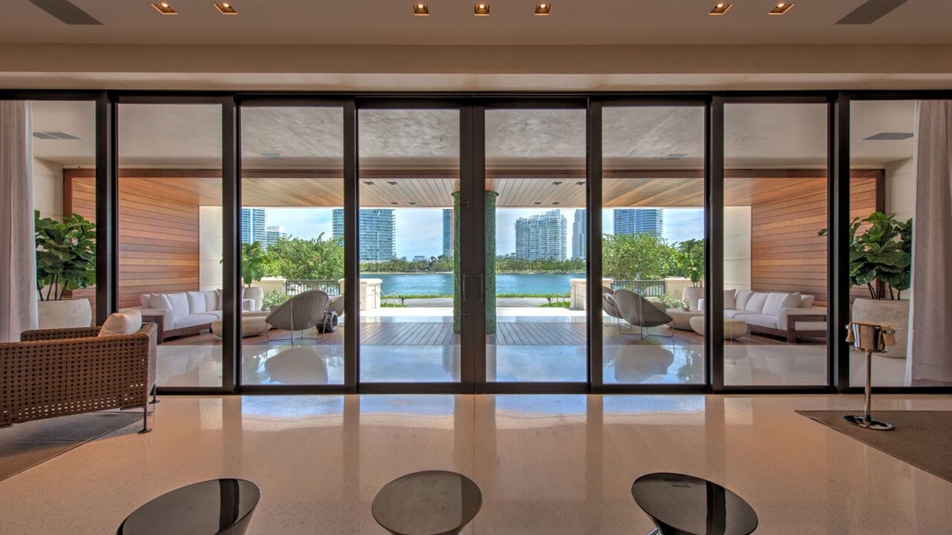 Glass-walled lounge at Palazzo del Sol, Fisher Island, presenting luxury and ultra luxury condos with large sliding doors opening to a covered waterfront terrace and skyline views.