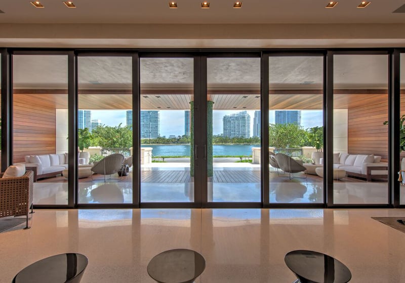 Glass-walled lounge at Palazzo del Sol, Fisher Island, presenting luxury and ultra luxury condos with large sliding doors opening to a covered waterfront terrace and skyline views.