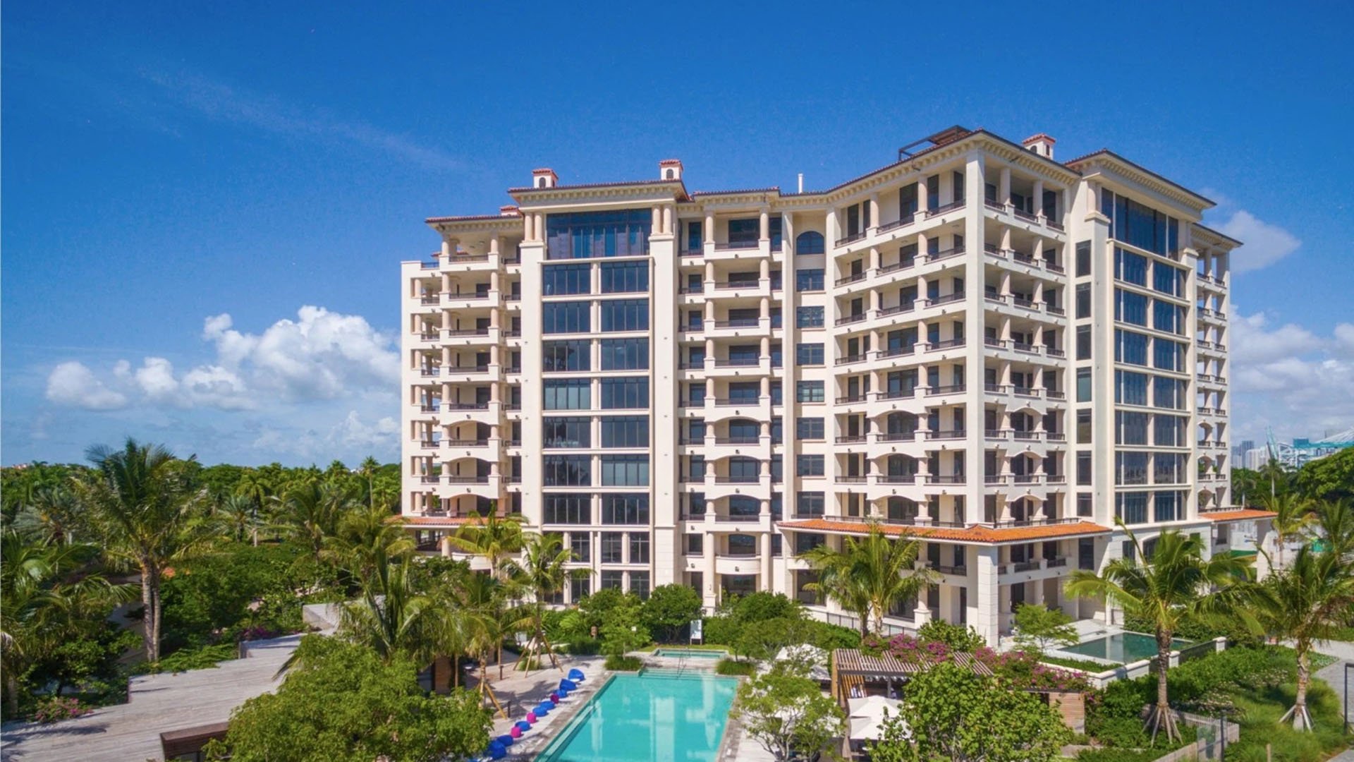 Exterior view of Palazzo del Sol, Fisher Island, highlighting luxury and ultra luxury condos with palm landscaping, a resort pool courtyard, and a refined mid-rise facade.