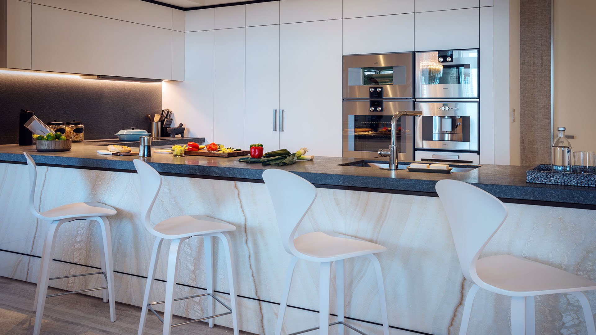 Minimal chef kitchen at Palazzo del Sol, Fisher Island, showcasing luxury and ultra luxury condos with black counters, white cabinetry, bar stools, and integrated appliances.