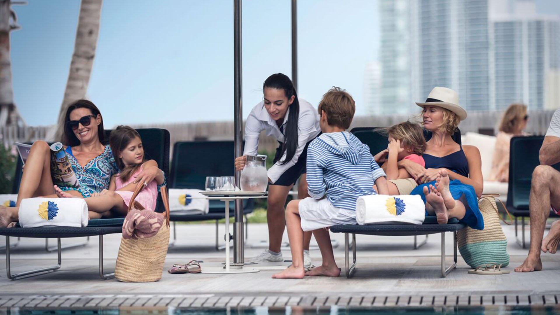 Poolside butler service at Palazzo del Sol, Fisher Island, highlighting luxury and ultra luxury condos with a family on sun loungers and attentive food and beverage service.