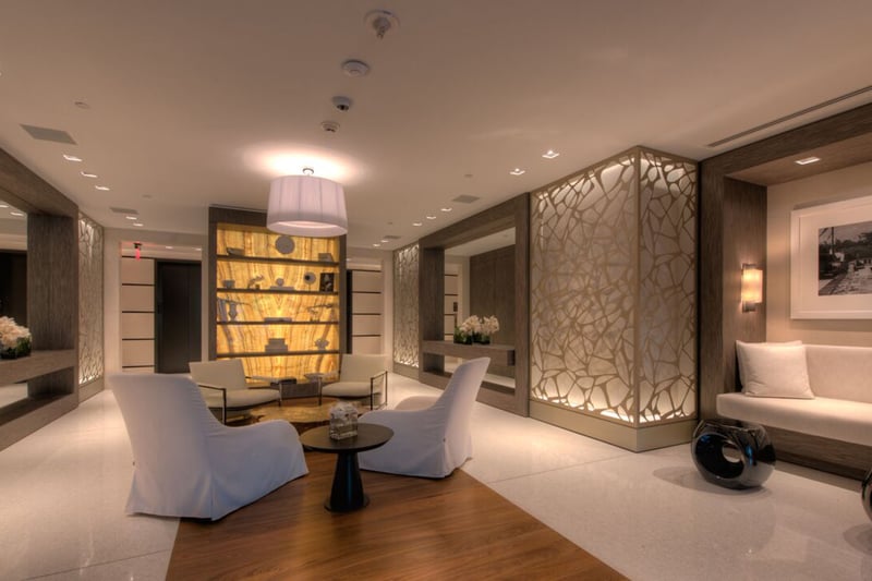 Reception lobby at Palazzo del Sol, Fisher Island, reflecting luxury and ultra luxury condos with backlit display shelving, sculpted wall panels, lounge seating, and a polished contemporary arrival.