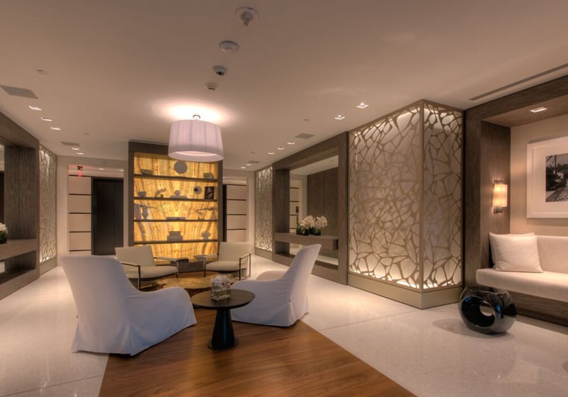 Reception lobby at Palazzo del Sol, Fisher Island, reflecting luxury and ultra luxury condos with backlit display shelving, sculpted wall panels, lounge seating, and a polished contemporary arrival.