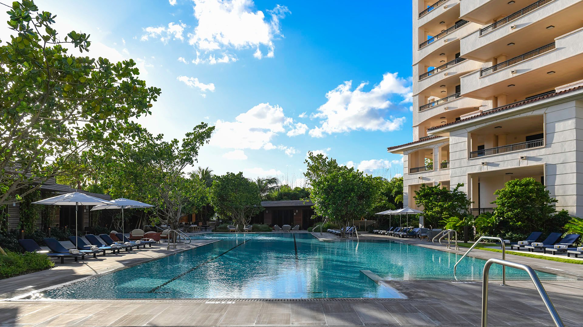 Palazzo della Luna in Fisher Island luxury and ultra luxury condos with a daytime pool terrace between the towers, loungers, umbrellas, and tropical greenery.