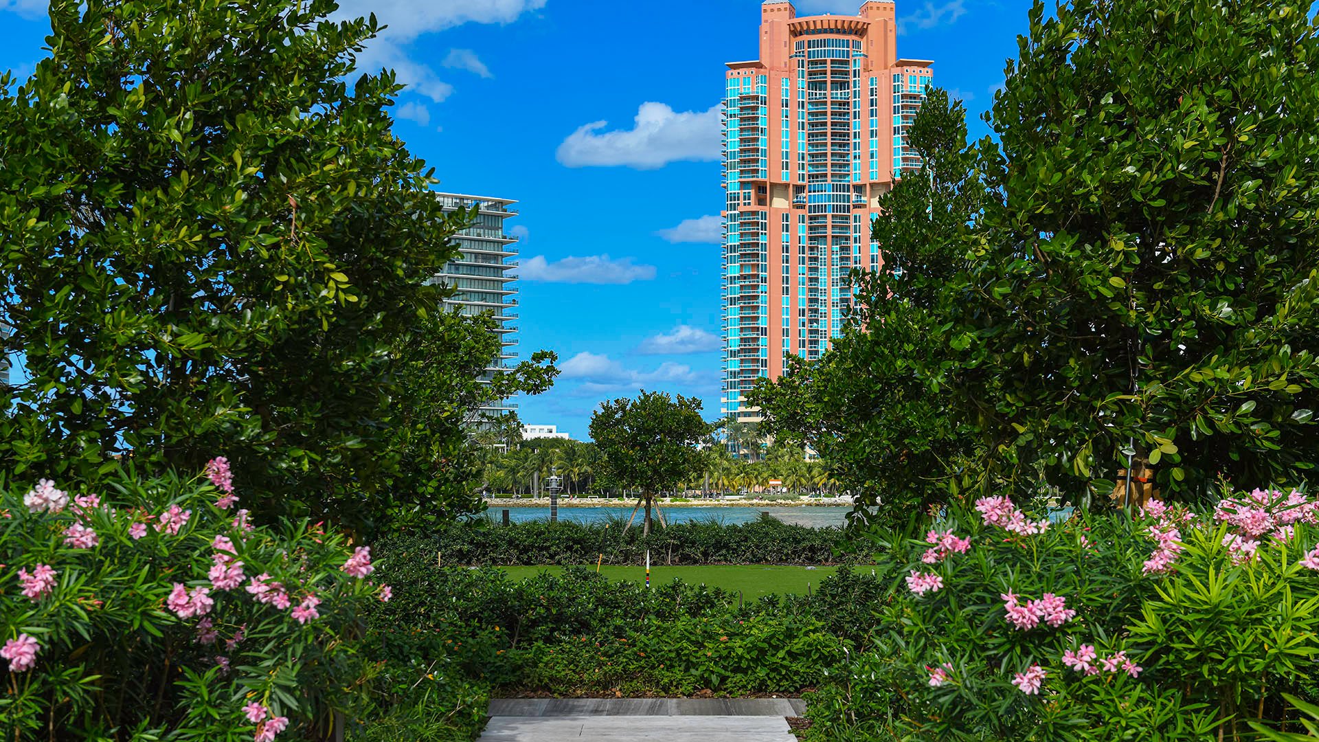 Palazzo della Luna in Fisher Island luxury and ultra luxury condos with a lush entry garden framed by flowering shrubs and a tower view beyond.