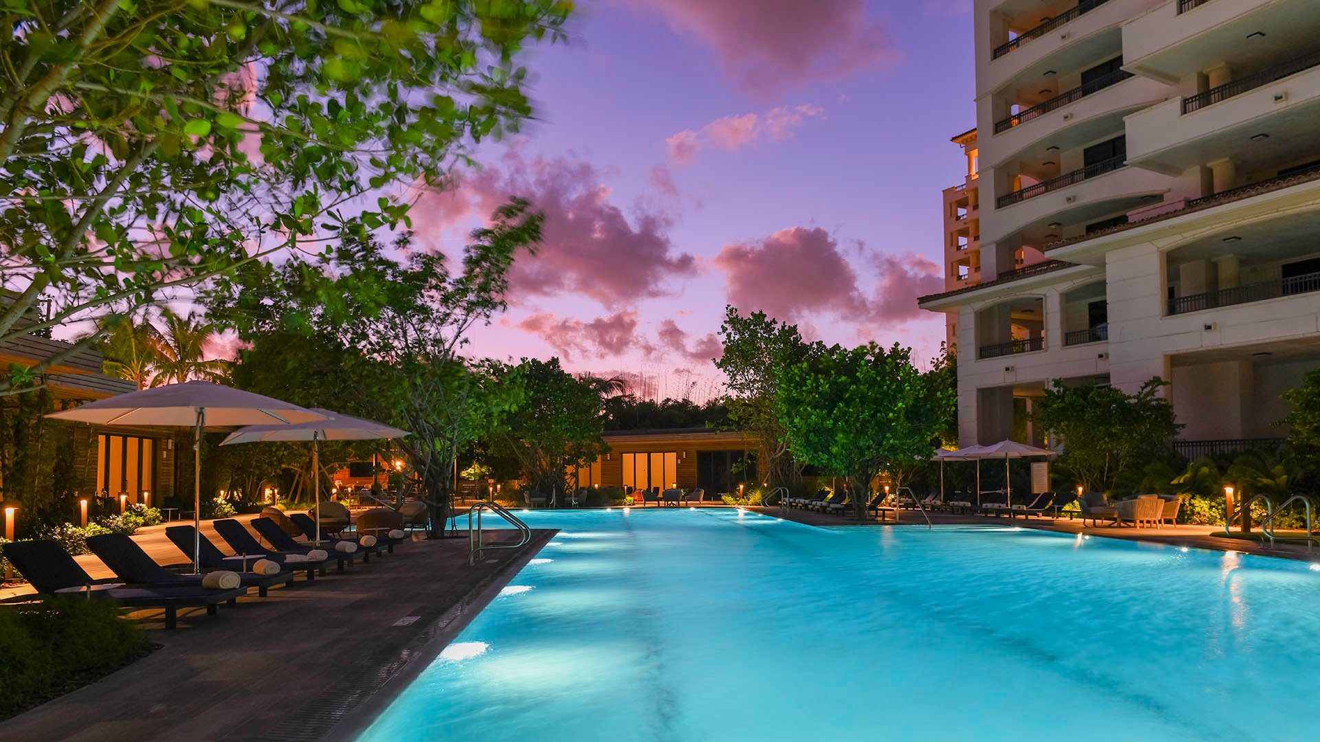 Palazzo della Luna in Fisher Island luxury and ultra luxury condos with a twilight pool terrace between the towers, underwater lighting, loungers, and a violet sky.