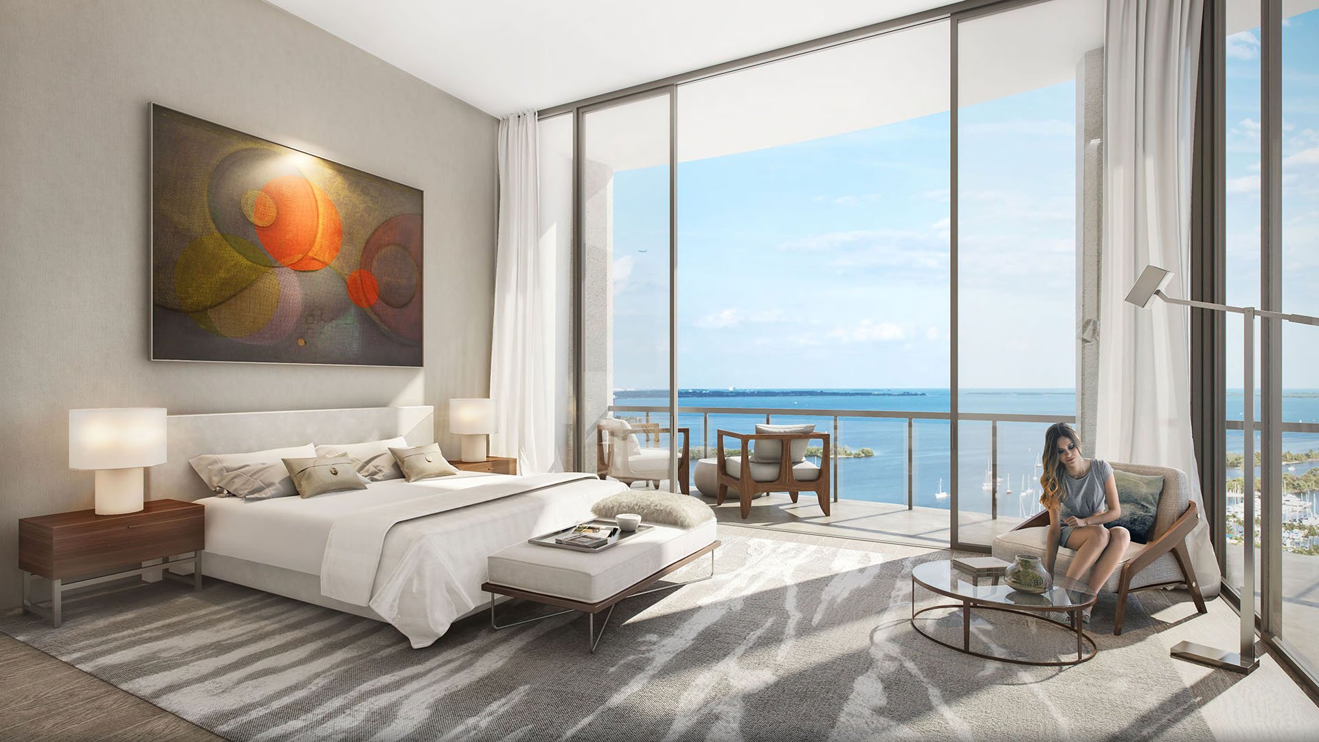 Primary bedroom with a reading chair, large art piece and a glass-lined bay view balcony at Park Grove in Coconut Grove, created for luxury and ultra luxury condos living.