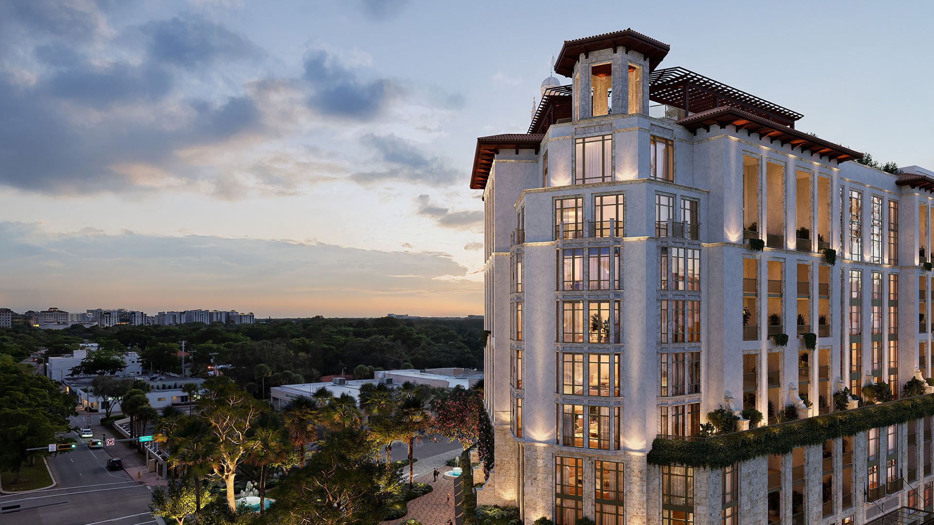 Ponce Park Residences Coral Gables, Miami twilight aerial of corner facade with lit windows and rooftop pergolas, highlighting luxury and ultra luxury preconstruction condos overlooking tree-lined city views.
