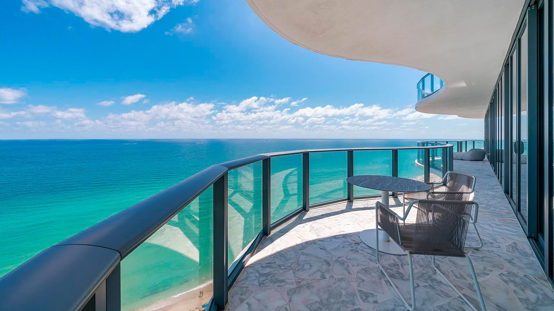 Curved beachfront balcony at Regalia in Sunny Isles Beach with bistro seating and sweeping ocean views from luxury and ultra luxury condos.