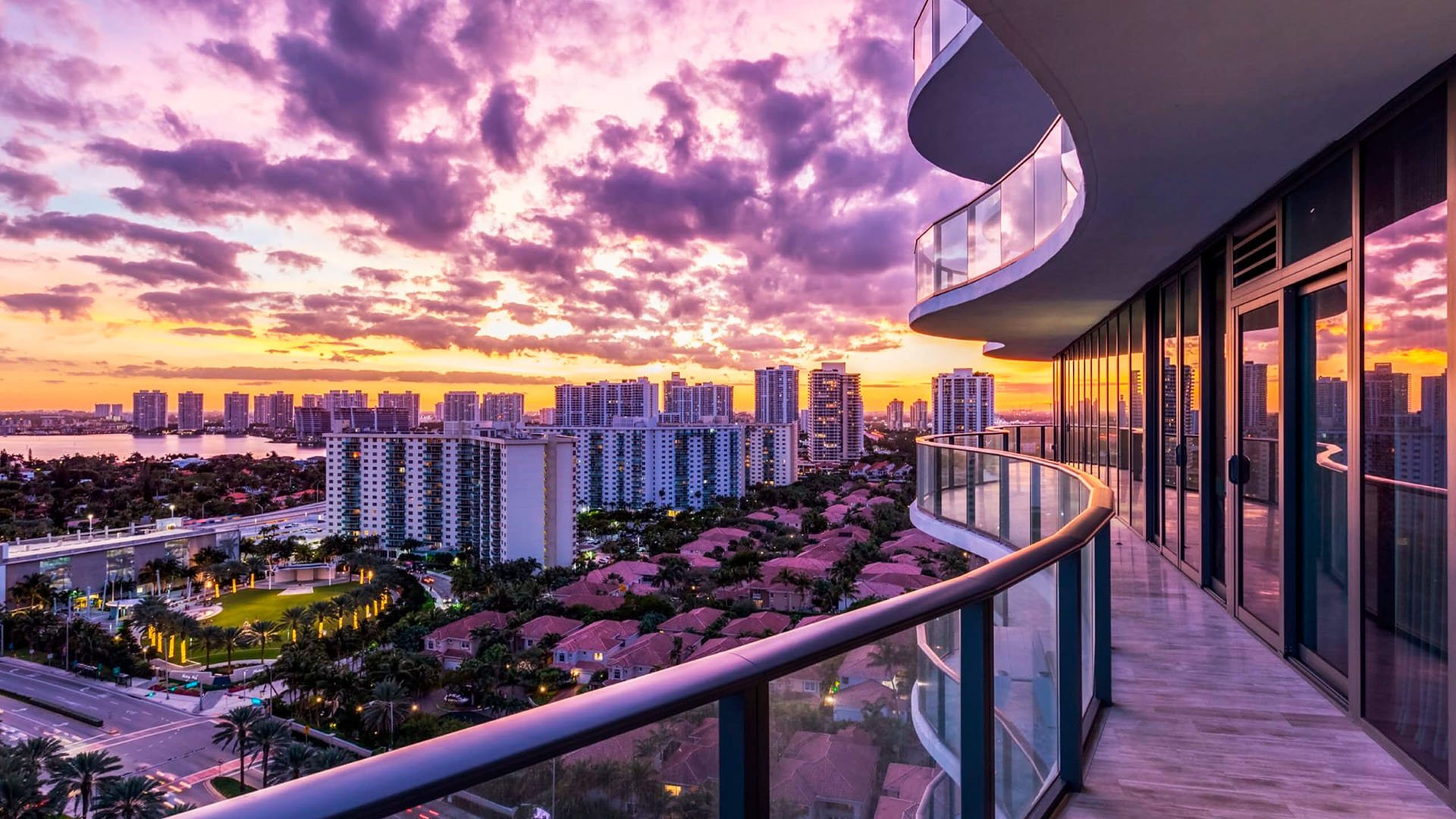Curved sunset balcony at Regalia in Sunny Isles Beach with a glowing skyline view and floor-to-ceiling glass wrapping luxury and ultra luxury condos.