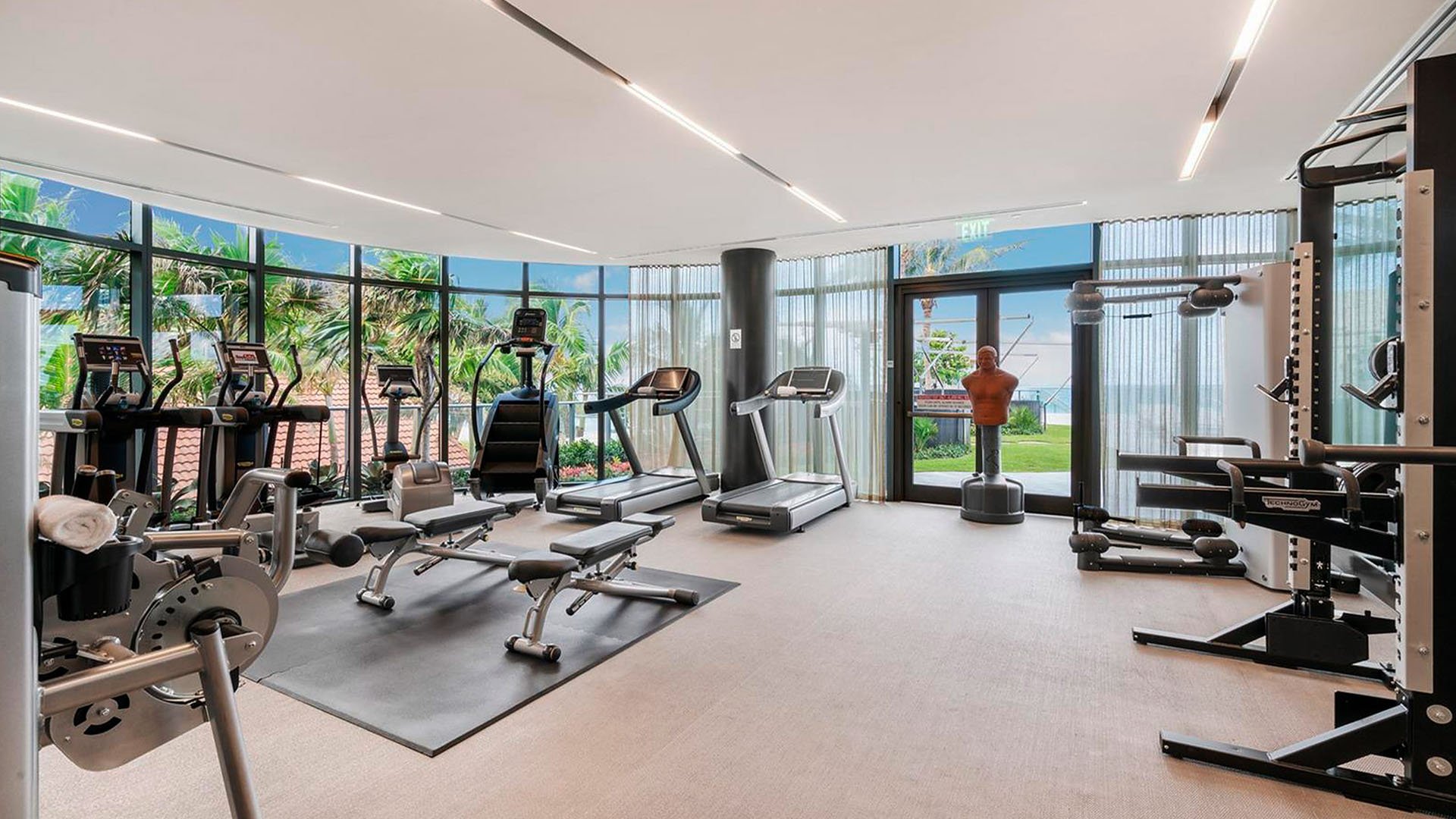 Fitness center at Regalia in Sunny Isles Beach with cardio and strength equipment, wide windows, and garden views for luxury and ultra luxury condos.