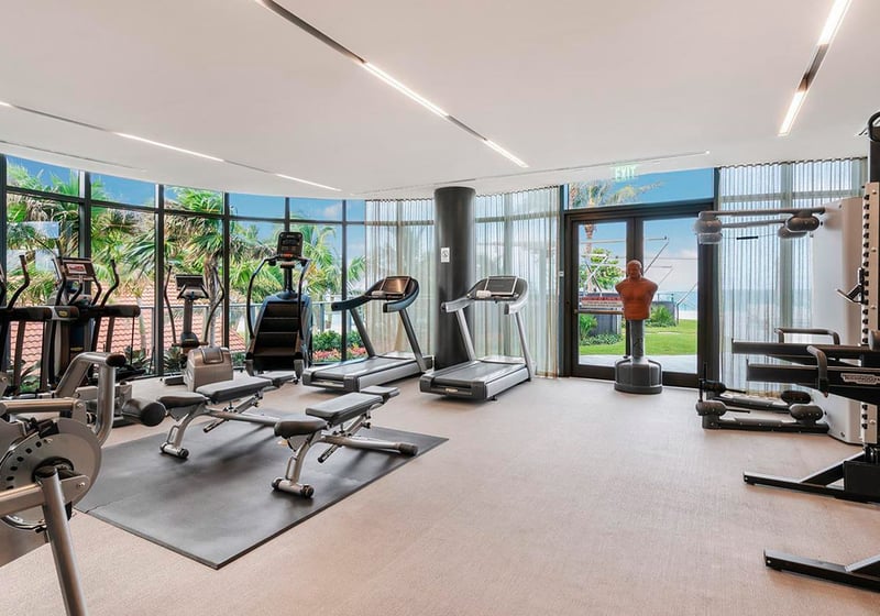 Fitness center at Regalia in Sunny Isles Beach with cardio and strength equipment, wide windows, and garden views for luxury and ultra luxury condos.