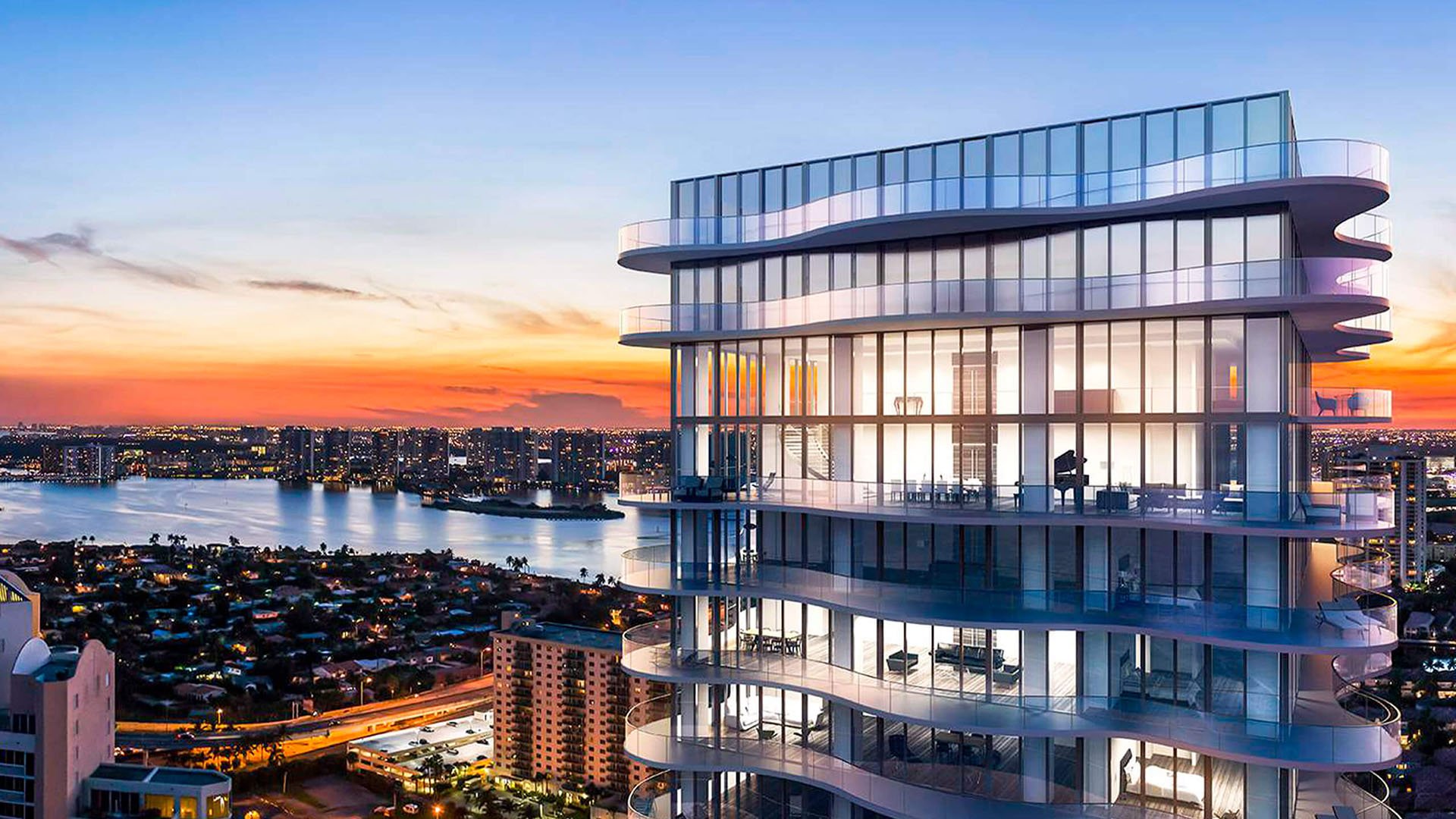 Glass upper levels at Regalia in Sunny Isles Beach glowing at sunset above the bay skyline, showcasing luxury and ultra luxury condos.
